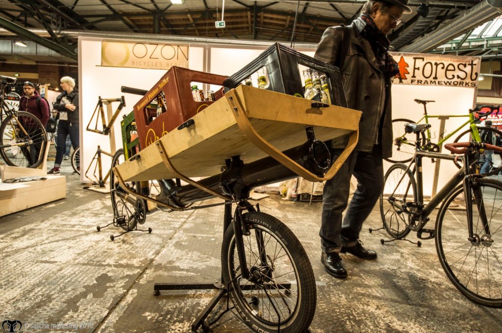 a bicycle parked Ozone-Cyclery bei denen Ihr in mehrtägigen Workshops Euer eigenes individuelles Bambusrad bauen könnt, zeigen ein ziemlich außergewöhnliches Cargobike. Sieht ein bißchen aus wie ein Kanonenrohr, findet Ihr nicht?on the side of a building