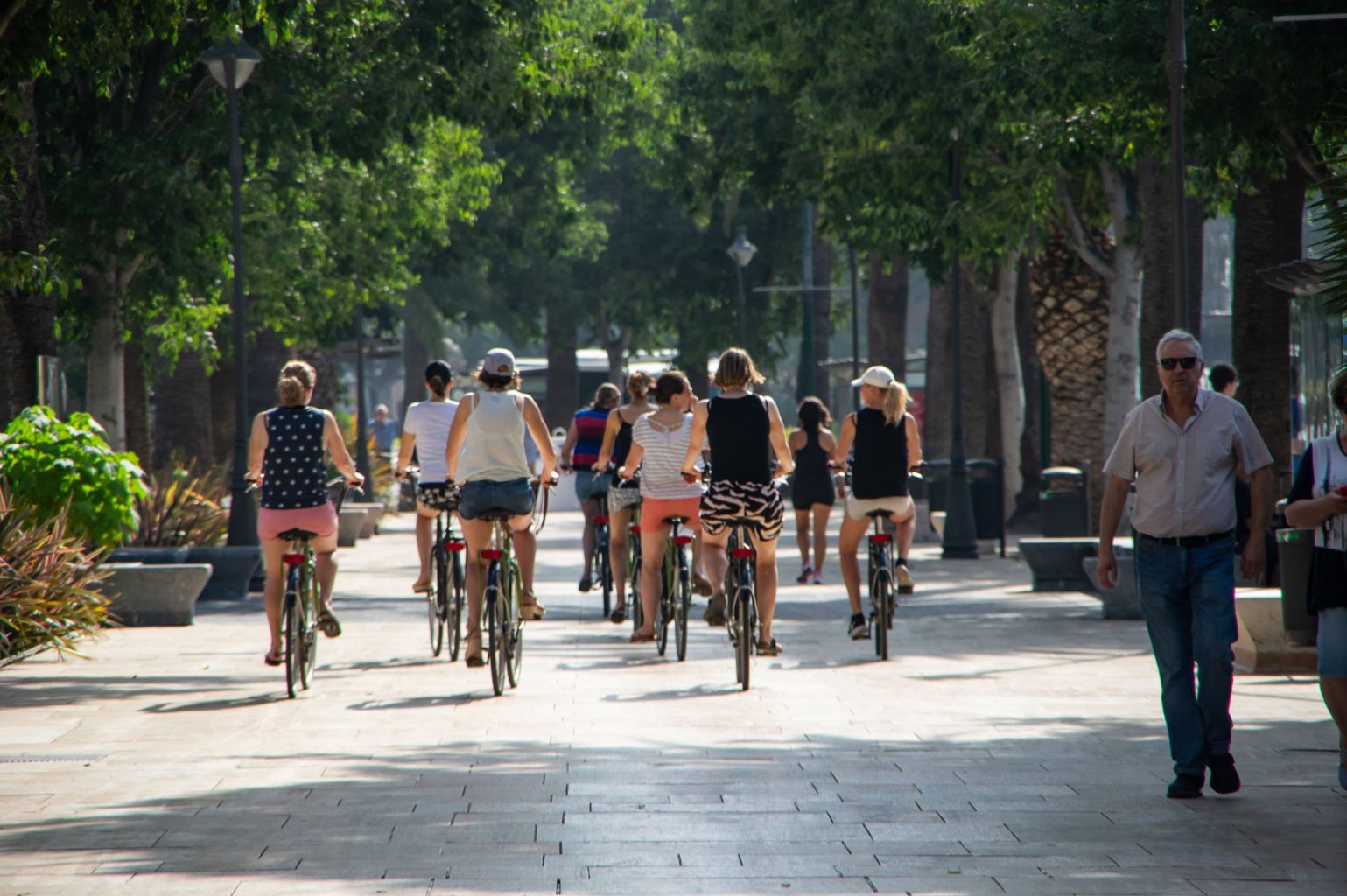Group of a dozen cyclists riding on the sidewalk of PAseo de Parque in Malaga.