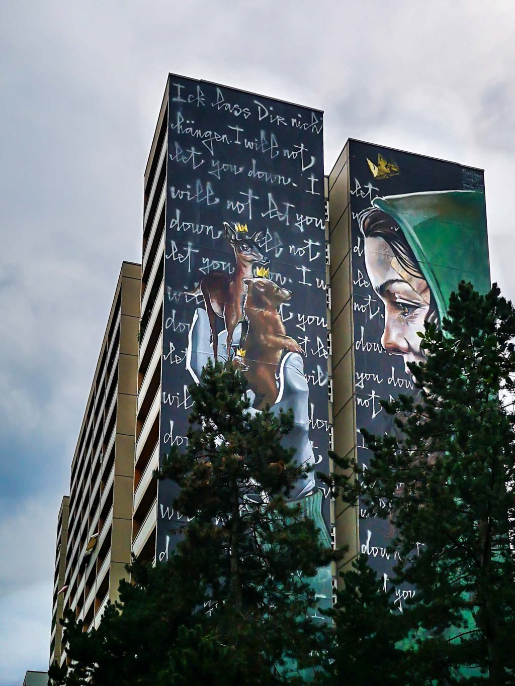 Mural in Berlin: a girl with a hoody holds a deer and a bear in her gloved hand. Mural by Herakut and Nuno Viegas.