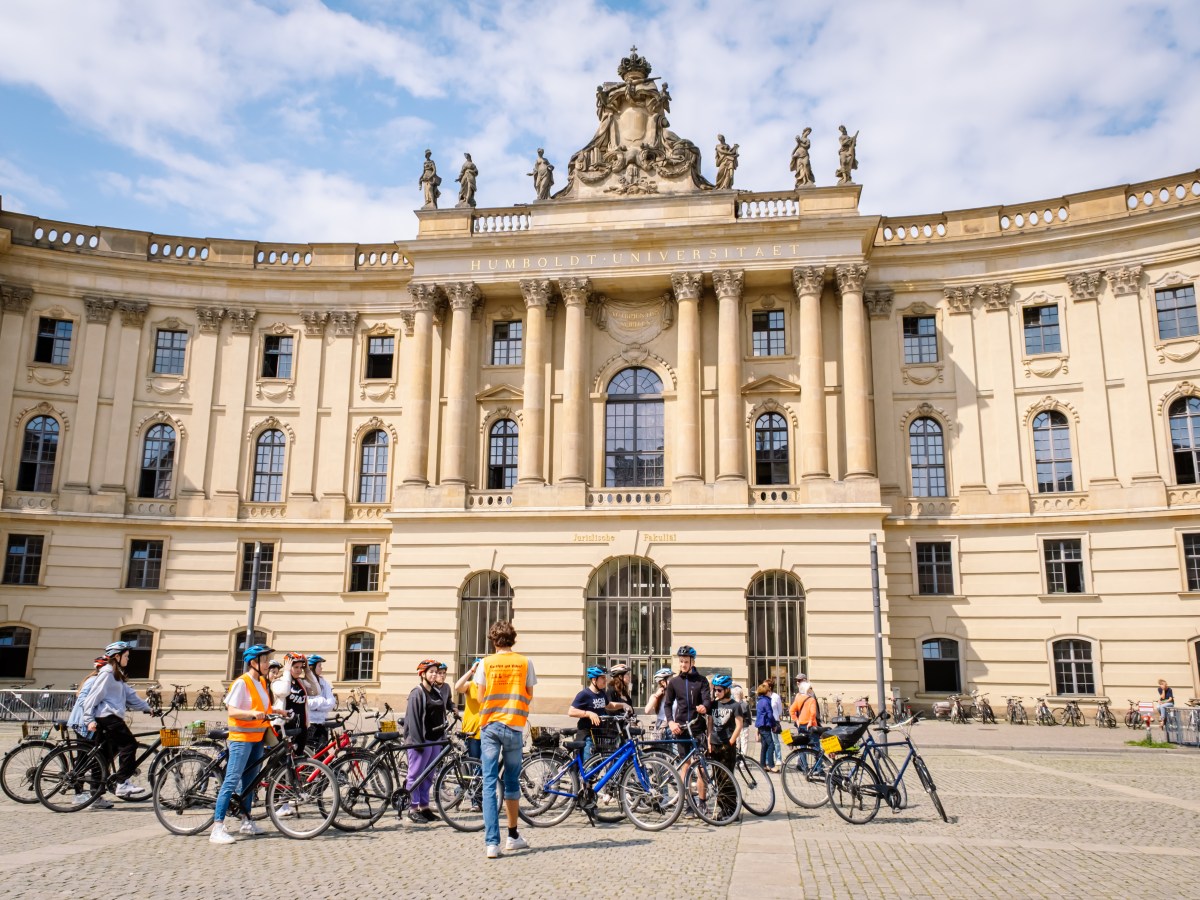 Cyclists gathered in front of a historic building with statues and columns.
