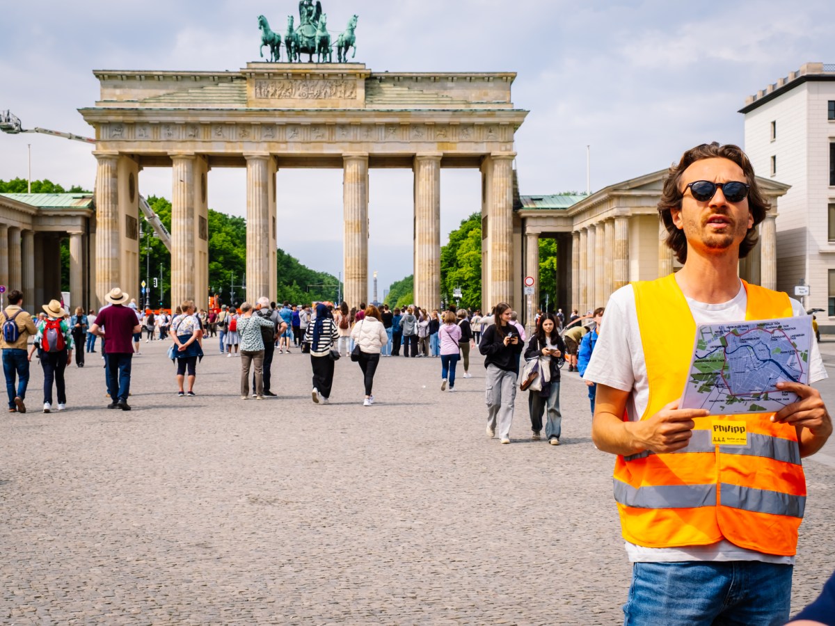 Tour guide with map near Brandenburg Gate, Berlin, crowded with tourists.